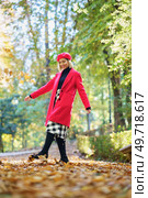 Full body of positive female in red clothes and beret walking on pathway with withered leaves in autumn park with trees. Fashionable woman on path with fallen leaves. Стоковое фото, агентство Ingram Publishing / Фотобанк Лори