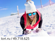 Smiling young female blonde in beanie cap polarized sunglasses, looking at camera while leaning on hands and doing push ups on rock against blurred wooden pillars fence in daylight. Smiling young woman in beanie wool cap and sunglasses warming up on snow. Стоковое фото, агентство Ingram Publishing / Фотобанк Лори