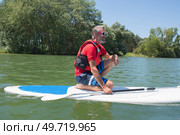 mature attractive rider contemplating nature sitting on paddle board. Стоковое фото, агентство Ingram Publishing / Фотобанк Лори