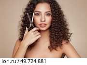 Beautiful young woman with a bright makeup and a afro  hair holds metal scissors. Model with curly hair. Hair salon, haircut. Care and beauty hair products. Perfect make-up. Стоковое фото, агентство Ingram Publishing / Фотобанк Лори