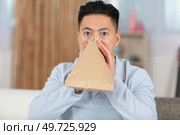 man sitting on sofa vomiting into paper bag at home. Стоковое фото, агентство Ingram Publishing / Фотобанк Лори
