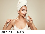 Image of a young happy positive woman in towel and with cosmetic patches on the eyes, brushing her teeth isolated over beige wall background. Стоковое фото, агентство Ingram Publishing / Фотобанк Лори