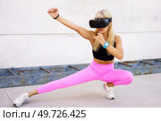 Full body of fit strong female athlete in sportswear and VR headset performing wushu fighting stance while experiencing virtual world. Sportswoman in VR headset practicing kung fu. Стоковое фото, агентство Ingram Publishing / Фотобанк Лори