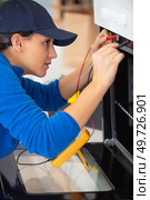 young woman checks oven malfunction with multimeter. Стоковое фото, агентство Ingram Publishing / Фотобанк Лори