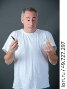 undecided man choosing between cigarettes and vaporiser. Стоковое фото, агентство Ingram Publishing / Фотобанк Лори
