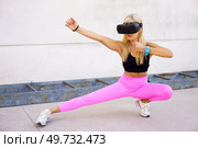 Full body of fit female in VR goggles performing kung fu fighting stance while practicing martial arts during virtual training outdoors. Strong sportswoman practicing martial arts in VR headset. Стоковое фото, агентство Ingram Publishing / Фотобанк Лори