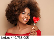 Beautiful portrait of an African girl with a heart shaped lollipop. Valentine’s Day. Symbol of love. Стоковое фото, агентство Ingram Publishing / Фотобанк Лори