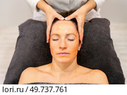 Crop cosmetologist doing facial massage of female customer, lying on towel with closed eyes and applying cleansing mask on face during skin care routine in beauty center. Crop cosmetologist massaging female client on face with cosmetic mask in beauty salon. Стоковое фото, агентство Ingram Publishing / Фотобанк Лори