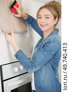 woman refurbishing kitchen cupboard with adhesive material. Стоковое фото, агентство Ingram Publishing / Фотобанк Лори