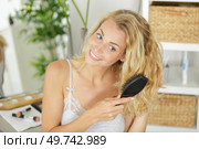 young woman brushing hair in front of a bathroom mirror. Стоковое фото, агентство Ingram Publishing / Фотобанк Лори
