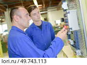 Senior and junior electricians looking at control box. Стоковое фото, агентство Ingram Publishing / Фотобанк Лори