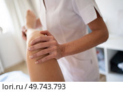 Crop anonymous female physiotherapist in medical uniform doing knee manipulation while treating leg of patient during physiotherapy session. Crop osteopath doing manipulations on leg of woman. Стоковое фото, агентство Ingram Publishing / Фотобанк Лори