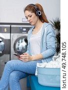 woman in laundromat using smartphone and wearing headphones. Стоковое фото, агентство Ingram Publishing / Фотобанк Лори