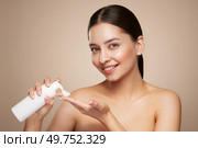A young woman shows off a bottle with a foam dispenser for washing. Daily skin care cosmetics advertisement. Studio shoot Beige background. Стоковое фото, агентство Ingram Publishing / Фотобанк Лори