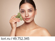 Beauty young woman doing skin care routine, scrapping, massage facial skin with jade gua sha scrapper, Facial treatment for anti aging and cosmetic cleaning. Стоковое фото, агентство Ingram Publishing / Фотобанк Лори