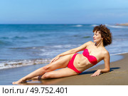 Full body of young curly woman with perfect body wearing pink bikini and lying on seashore in sunlight looking away. Slim woman in bikini suntanning on sandy beach. Стоковое фото, агентство Ingram Publishing / Фотобанк Лори