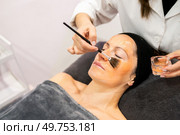From above of crop professional cosmetologist applying moisturizing product on face of calm female client with brush in beauty center. Beautician applying cosmetics on face of woman. Стоковое фото, агентство Ingram Publishing / Фотобанк Лори