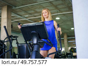 Low angle view horizontal photo with copy space of a blonde young caucasian woman walking exercising in elliptical machine in the gym. Woman walking exercising in elliptical machine in the gym. Стоковое фото, агентство Ingram Publishing / Фотобанк Лори