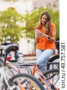 Vertical photo of a latin modern woman renting bike using mobile in the city. Woman renting bike using mobile in the city. Стоковое фото, агентство Ingram Publishing / Фотобанк Лори