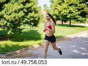 A fit woman in sportswear is jogging in a lush green park, enjoying the sunny day, maintaining a healthy lifestyle, and staying active to keep her vitality and wellness at peak levels. A young woman is jogging in the park on a sunny day, enjoying her workout in the fresh air surrounded by nature. Стоковое фото, агентство Ingram Publishing / Фотобанк Лори