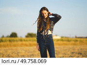 A young woman with curly hair poses in a vibrant bohemian outfit against a stunning sunset, highlighting her spirit of freedom and beauty, captivating every viewer with her enchanting presence. A young woman in a beautiful bohemian outfit poses gracefully in nature at sunset. Стоковое фото, агентство Ingram Publishing / Фотобанк Лори