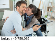 disabled woman kissing her husband holding a tablet. Стоковое фото, агентство Ingram Publishing / Фотобанк Лори