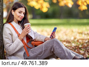 A young beautiful woman walks in the autumn park and talks on the phone. A girl with a smartphone takes photos in an autumn forest. Стоковое фото, агентство Ingram Publishing / Фотобанк Лори