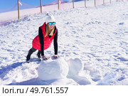 Full body of smiling young female blonde in beanie cap polarized sunglasses, looking away while leaning on hands and doing push ups on rock against wooden pillars fence in daylight. Happy woman warming up on snow terrain in winter. Стоковое фото, агентство Ingram Publishing / Фотобанк Лори