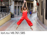 In an urban alley, a woman in a striking red jumpsuit catches attention with her energetic dance, showcasing her joyful spirit and inviting onlookers to share in her vibrant enthusiasm. A Joyful Dance Pose Captured in an Urban Alley An Exciting and Vibrant Fashion Scene. Стоковое фото, агентство Ingram Publishing / Фотобанк Лори