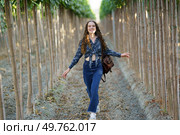 A young woman with long hair wearing a stylish outfit walks happily through a serene treelined path, embracing natures beauty. A Joyful and Radiant Young Woman Walking Happily in Nature Among Tall Trees and Greenery. Стоковое фото, агентство Ingram Publishing / Фотобанк Лори