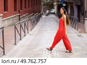 A stylish woman adorned in a vibrant red jumpsuit saunters gracefully along a scenic urban street, effortlessly showcasing her confidence and impeccable fashion sense for all to admire and appreciate. A woman dressed in a striking red jumpsuit is confidently walking down an urban street. Стоковое фото, агентство Ingram Publishing / Фотобанк Лори