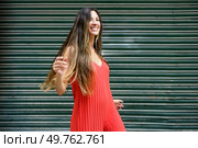 A lively young woman with long braided hair dances joyfully in a vibrant red dress, contrasting with a lush green backdrop, exuding an aura of energy and positivity that is contagious. A Joyful Young Woman Wearing a Bright Red Dress is Dancing Happily Against a Lush Green Background. Стоковое фото, агентство Ingram Publishing / Фотобанк Лори