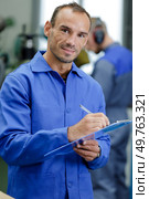 man writing on a clipboard in a garage. Стоковое фото, агентство Ingram Publishing / Фотобанк Лори