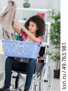 young happy woman on wheelchair putting clothes in basket. Стоковое фото, агентство Ingram Publishing / Фотобанк Лори