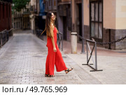 A stylish woman strolls with effortless grace down a charming city street, her vibrant red outfit radiating confidence and elegance, drawing the eyes of everyone around her with each step she takes. An Elegant Woman Dressed in a Stunning Red Outfit is Strolling Through the Bustling City Streets. Стоковое фото, агентство Ingram Publishing / Фотобанк Лори