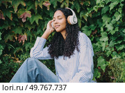 A young woman listens to her favorite music using headphones, fully immersed in enjoying a perfect moment of tranquility and peace in a stunning and beautiful natural setting that surrounds her. A Young Woman is Enjoying Her Favorite Music with Headphones While Surrounded by Lush Greenery. Стоковое фото, агентство Ingram Publishing / Фотобанк Лори