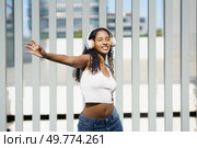 A young woman dances joyfully outdoors to an upbeat track, wearing trendy headphones and an eyecatching outfit that reflects joy, freedom, and vitality through her energetic movements. A Joyful Young Woman Dancing Outdoors While Wearing Stylish Headphones and Enjoying Life. Стоковое фото, агентство Ingram Publishing / Фотобанк Лори