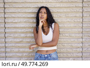 A thoughtful and introspective young woman with beautiful curly hair poses gracefully against a textured wall, showcasing a captivating moment of deep contemplation and reflection about life. A Thoughtful Young Woman Posing Gracefully Against a Textured Wall in Natural Light. Стоковое фото, агентство Ingram Publishing / Фотобанк Лори
