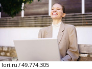A confident businesswoman in a stylish outfit smiles as she works on her laptop outdoors, showcasing a productive work environment where innovation and creativity thrive in nature. A Smiling Businesswoman is Enjoying Her Work on a Laptop While Sitting Outdoors in Nature. Стоковое фото, агентство Ingram Publishing / Фотобанк Лори