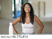In a welcoming setting, a confident young woman with curly hair and stylish glasses beams a smile that spreads positivity and warmth, uplifting everyone with her selfassurance and charisma. A Confident Young Woman Happily Smiling at the Camera While in a Casual and Relaxed Setting. Стоковое фото, агентство Ingram Publishing / Фотобанк Лори