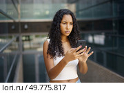 A young woman with curly hair appears quite concerned, and distracted as she texts on her smartphone while surrounded by the hustle and bustle of an urban environment filled with activity. A young woman is completely engrossed in her smartphone as she messages outside during the day. Стоковое фото, агентство Ingram Publishing / Фотобанк Лори