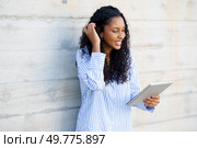 A cheerful young woman in a colorful striped shirt is engaged with her tablet, showcasing her enthusiasm for modern technology and the resources it provides for her daily activities. A Happy Young Woman Engaged with Her Tablet in a Stylish and Modern Indoor Setting. Стоковое фото, агентство Ingram Publishing / Фотобанк Лори