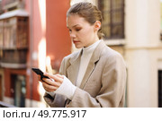 A fashionable woman in a beige blazer and cozy turtleneck engages with her smartphone in a vibrant urban setting, embodying modernity, elegance, grace, and poise with every interaction. A fashionable young woman skillfully using her smartphone while outdoors in daylight. Стоковое фото, агентство Ingram Publishing / Фотобанк Лори
