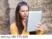 In a beautiful outdoor setting, a young woman in a colorful sweater focuses on her tablet, showcasing the balance between modern tech and concentration, reflecting her dedication to learning. A Young Woman Engaged in Using a Tablet Outdoors, Displaying Strong Focus and Intention. Стоковое фото, агентство Ingram Publishing / Фотобанк Лори
