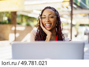 A cheerful young woman with an infectious smile enjoys her work on a laptop at a vibrant outdoor cafe, fully engaged and radiating positivity as she immerses herself in her creative task. A happy young woman is diligently working on her laptop at a vibrant outdoor cafe setting. Стоковое фото, агентство Ingram Publishing / Фотобанк Лори