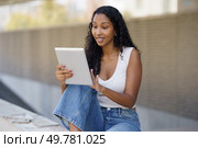 A young woman is happily enjoying her time outdoors while using her tablet, beautifully embodying a carefree lifestyle in a casual setting that perfectly reflects her vibrant and lively personality. A young woman is actively engaged with her digital tablet while sitting outdoors in the sunlight. Стоковое фото, агентство Ingram Publishing / Фотобанк Лори