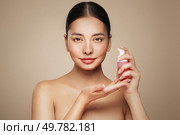 A young woman shows off a bottle with a foam dispenser for washing. Daily skin care cosmetics advertisement. Studio shoot Beige background. Стоковое фото, агентство Ingram Publishing / Фотобанк Лори