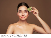 Beauty young woman doing skin care routine, scrapping, massage facial skin with jade gua sha scrapper, Facial treatment for anti aging and cosmetic cleaning. Стоковое фото, агентство Ingram Publishing / Фотобанк Лори