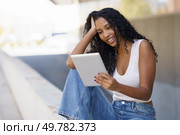 A young woman with curly hair joyfully uses her tablet outdoors, fully immersed in a blissful moment, surrounded by an inspiring and uplifting environment that radiates positivity. A Joyful and Beautiful Young Woman is Engaged with Her Tablet While Outdoors in Nature. Стоковое фото, агентство Ingram Publishing / Фотобанк Лори