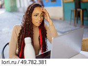 A young woman with intricate braids and stylish glasses looks worried while working on her laptop at a caf. Stressful moments in a vibrant outdoor setting. Concerned Woman Working on Laptop in a Caf. Стоковое фото, агентство Ingram Publishing / Фотобанк Лори